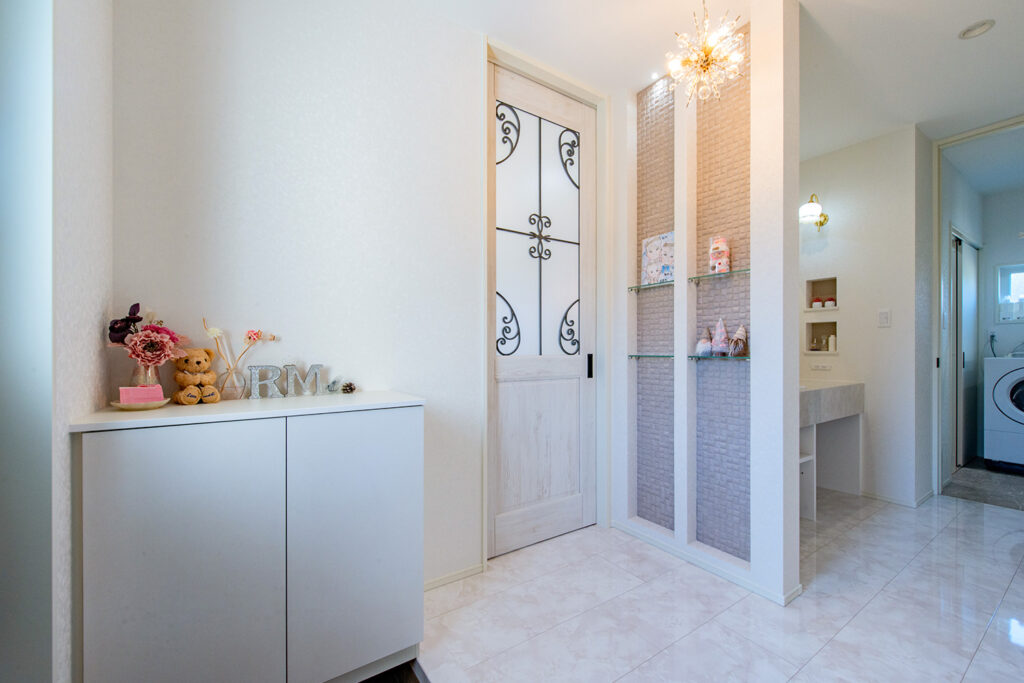 やさしい白に包まれた、飾る楽しみのある玄関。二連のガラス棚ニッチに並べたお気に入りを、照明がやさしく引き立てます。