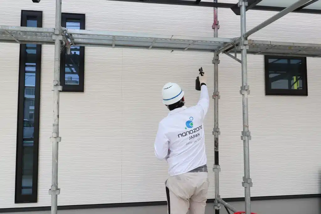 作業員が北側外壁にナノゾーンコートをスプレーガンで吹き付けている施工中の様子