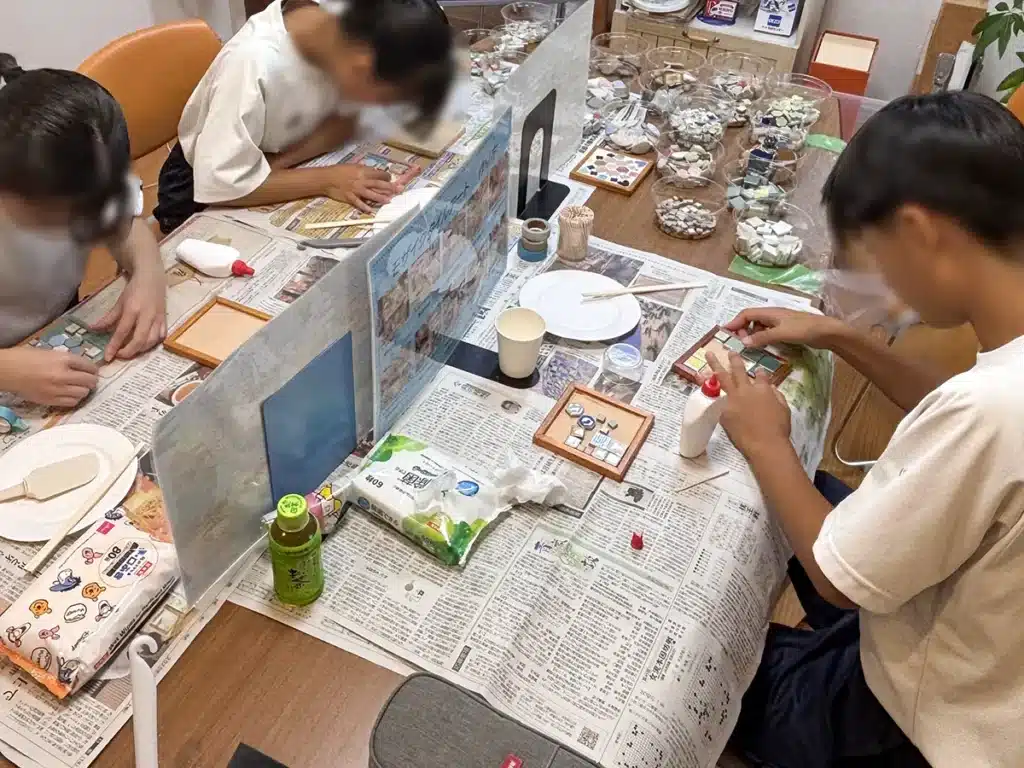 中学生3名がモザイクタイルを使ってオリジナルのコースターを制作している職場体験の様子